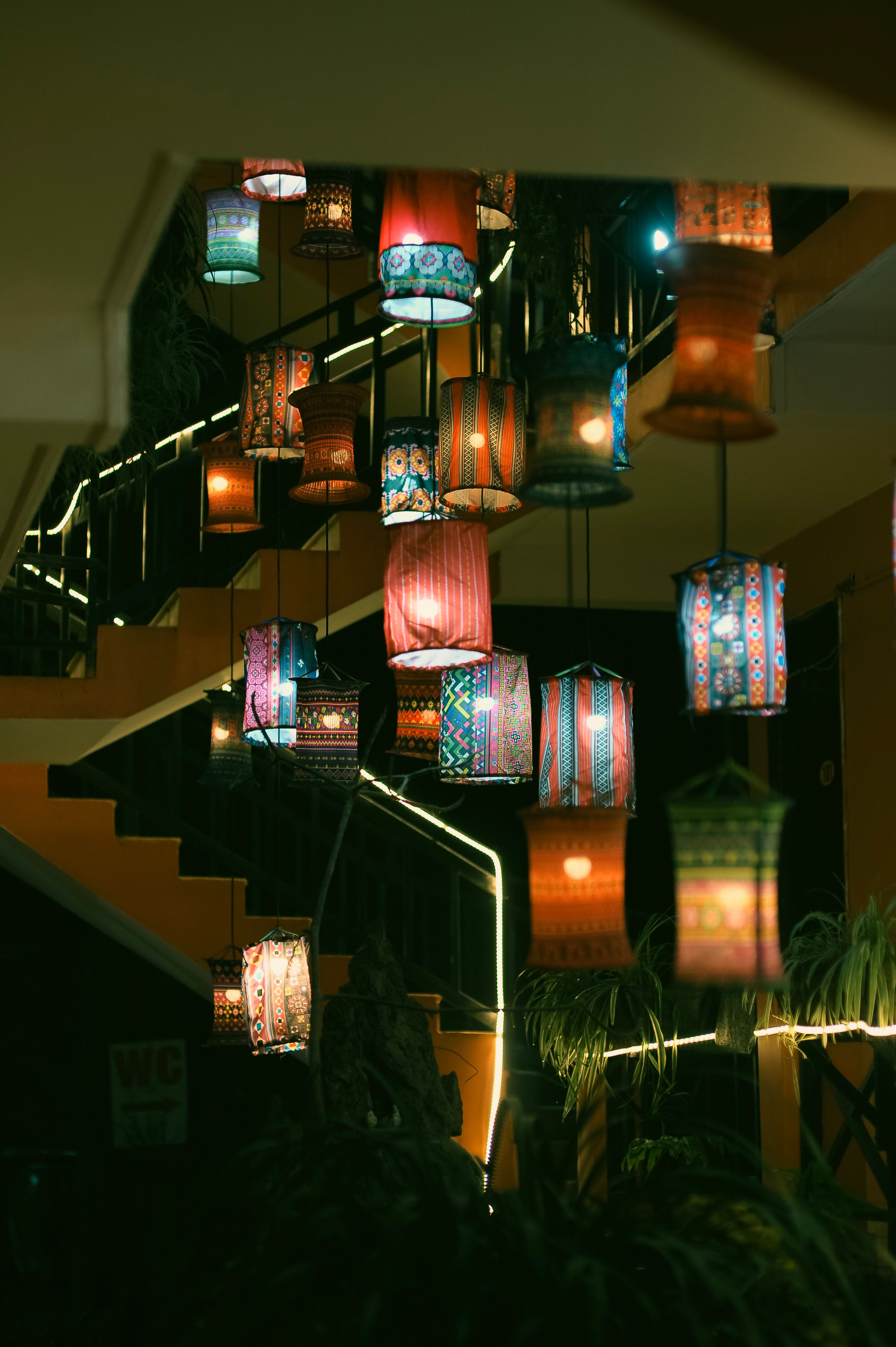 Vibrant hanging lanterns illuminate an indoor staircase with warm light.