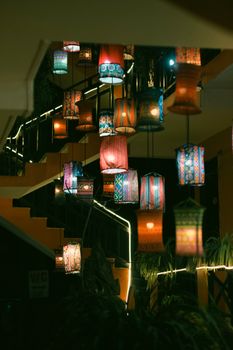 Vibrant hanging lanterns illuminate an indoor staircase with warm light.