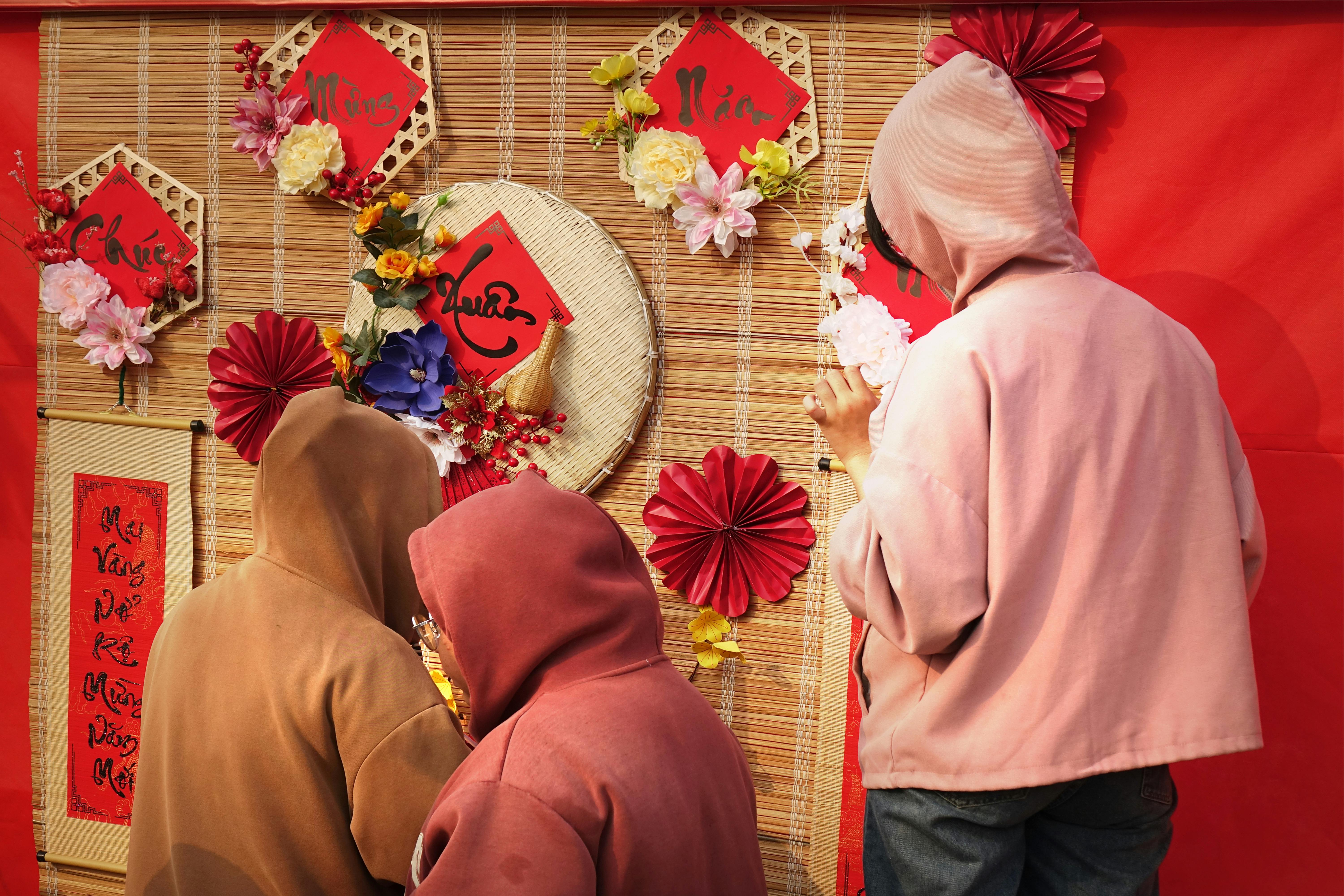 무료 후드티를 입은 세 사람이 축제 행사에서 화려한 아시아풍 장식 벽을 감상하고 있다. 스톡 사진