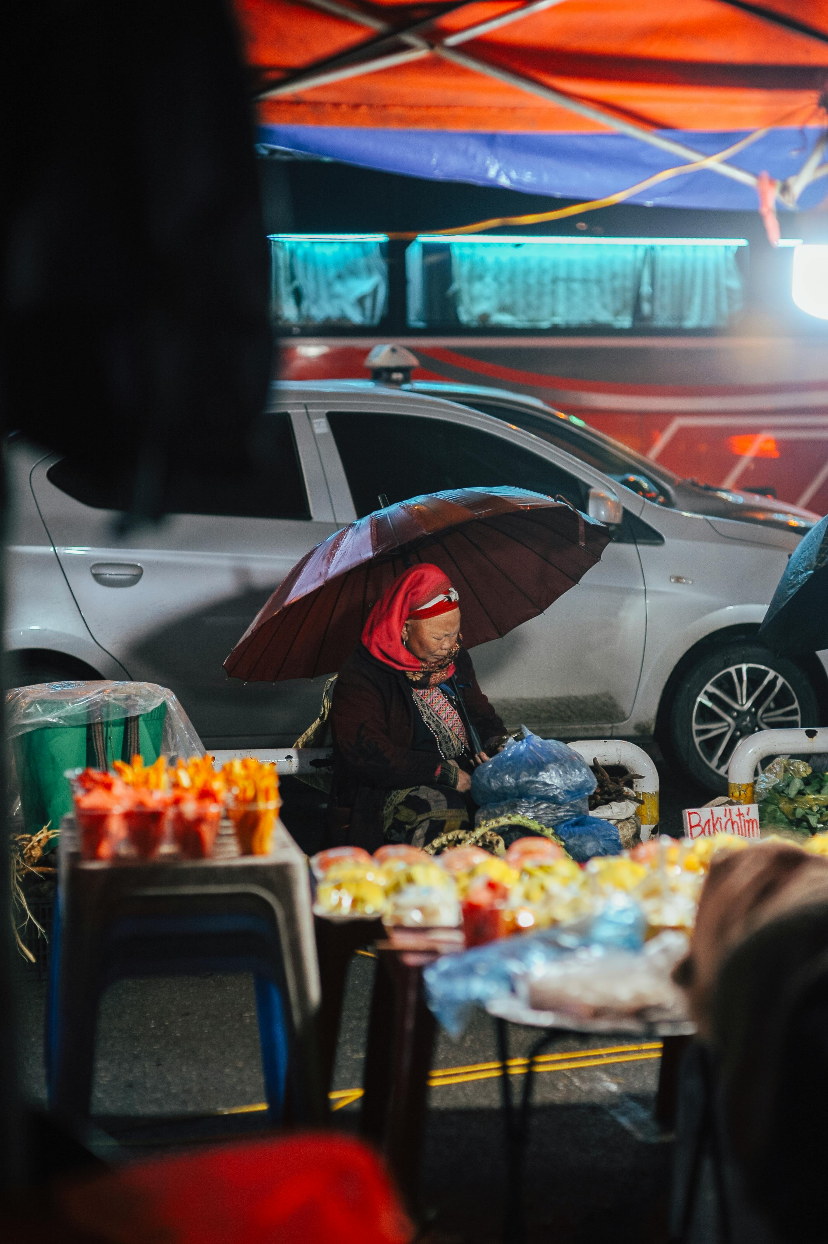 ฟรี พ่อค้าแม่ค้าขายผักผลไม้สดใต้ร่มสีสันสดใสในบรรยากาศตลาดกลางคืนที่คึกคัก คลังภาพถ่าย