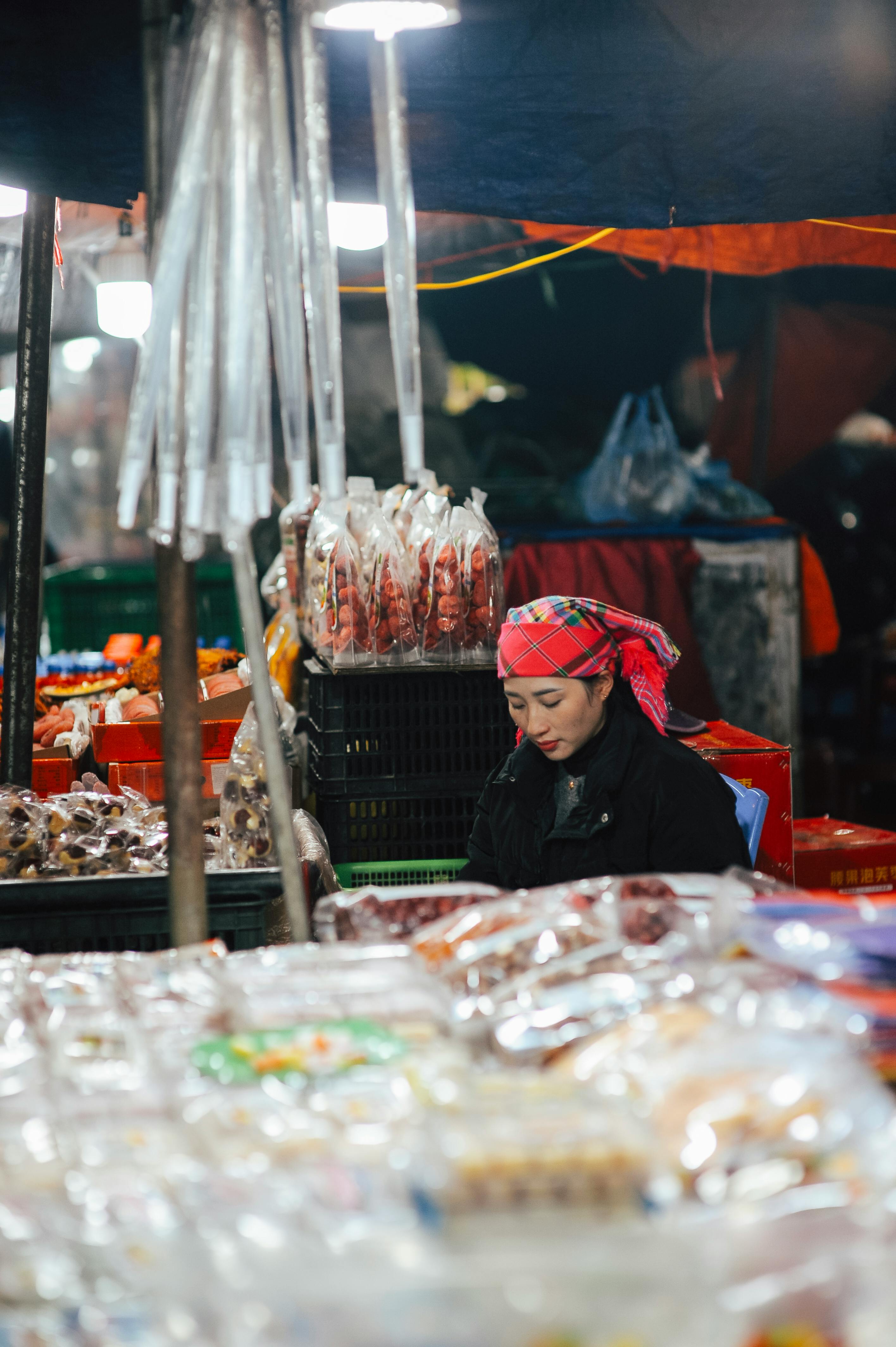 免费 在热闹的夜市上，一位戴着红色头巾的女子全神贯注地照看着自己的摊位。 素材图片