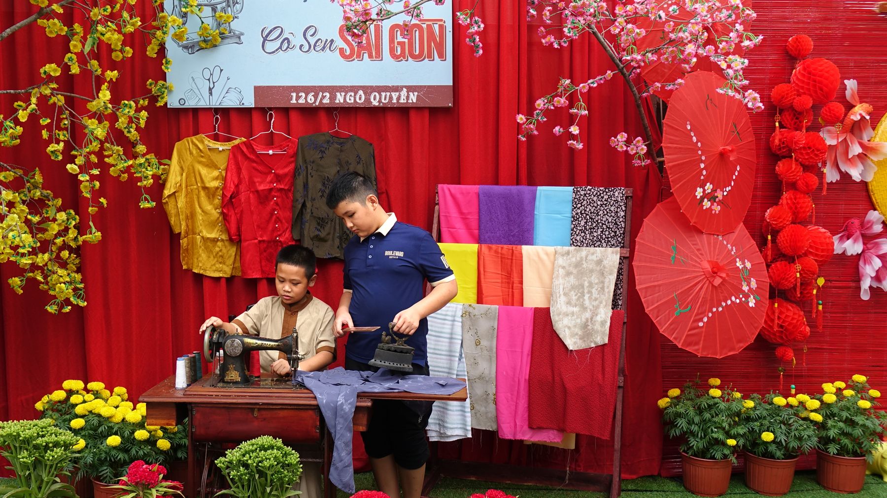 Two boys engaged in traditional sewing at a colorful Vietnamese market stall.