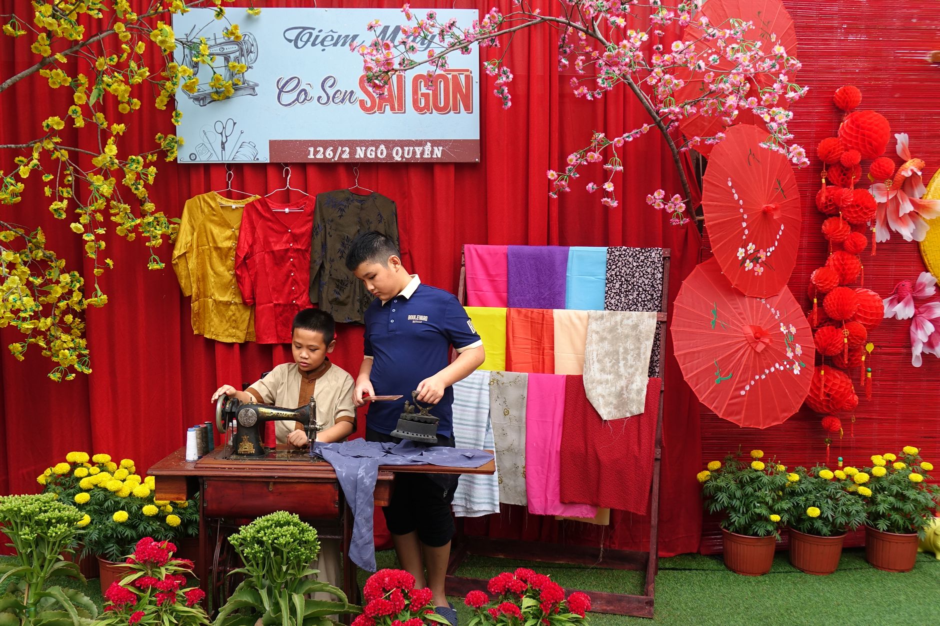 Two boys engaged in traditional sewing at a colorful Vietnamese market stall.
