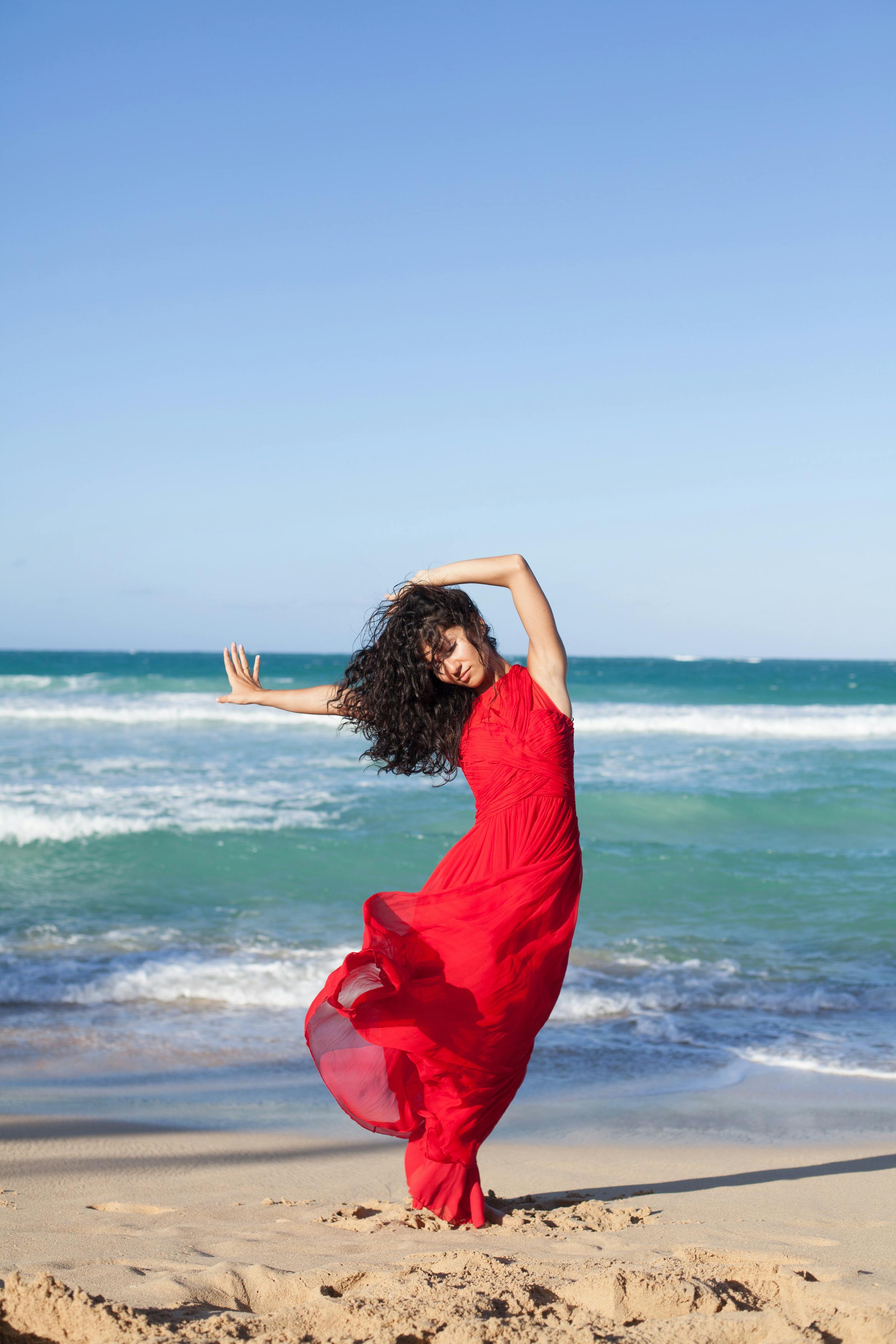 ฟรี ภาพบันทึกการเคลื่อนไหวอันงดงามของหญิงสาวในชุดเดรสสีแดงพลิ้วไหวขณะเต้นรำบนชายหาดที่แสงแดดส่องประกายในสาธารณรัฐโดมินิกัน คลังภาพถ่าย