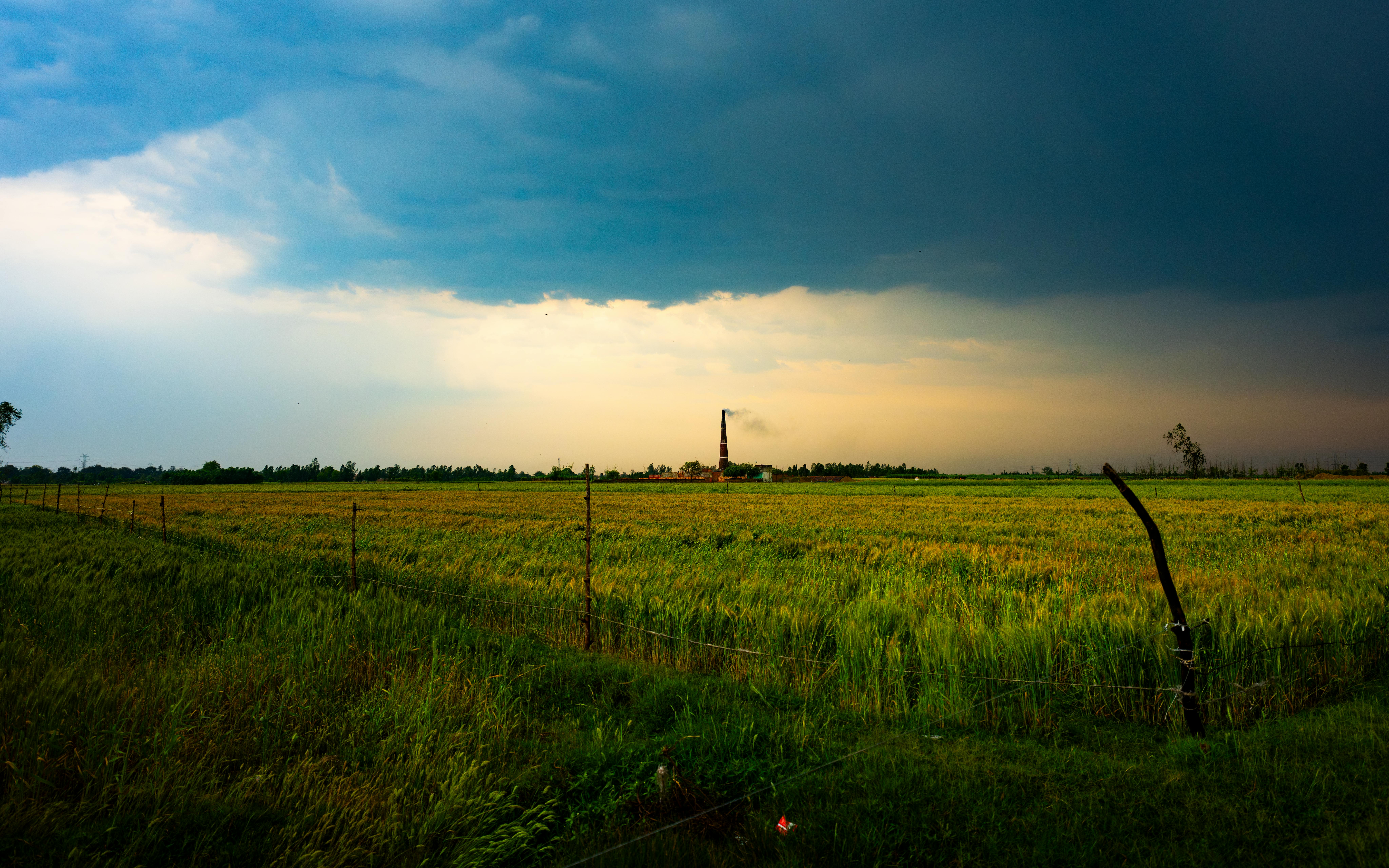 Zadarmo Rozľahlé pšeničné pole pod dramatickou oblohou s týčiacim sa komínom v diaľke. Fotka z fotobanky