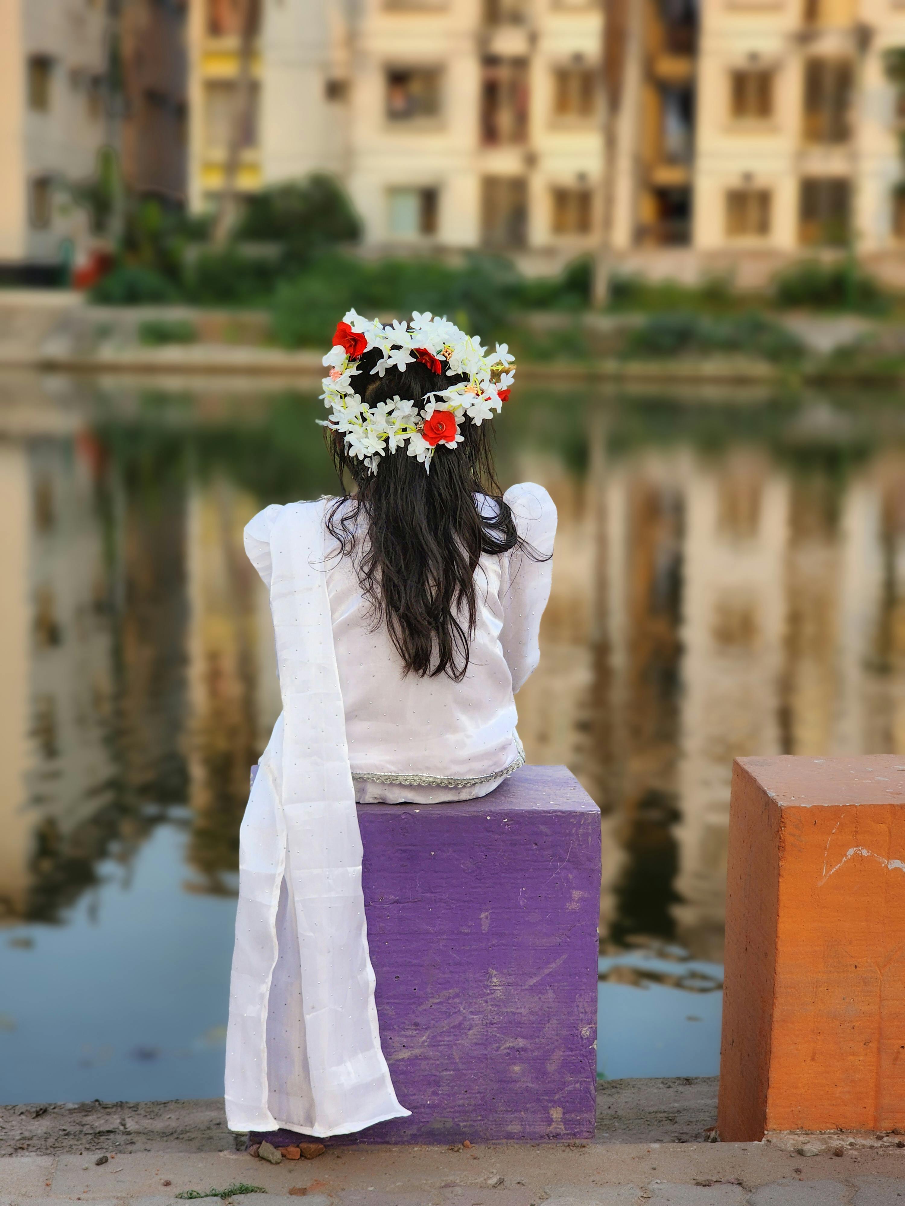 免费 阳光明媚的日子里，一位身穿白色连衣裙、头戴花冠的年轻女孩站在河边，镜头从她的背影拍摄。 素材图片