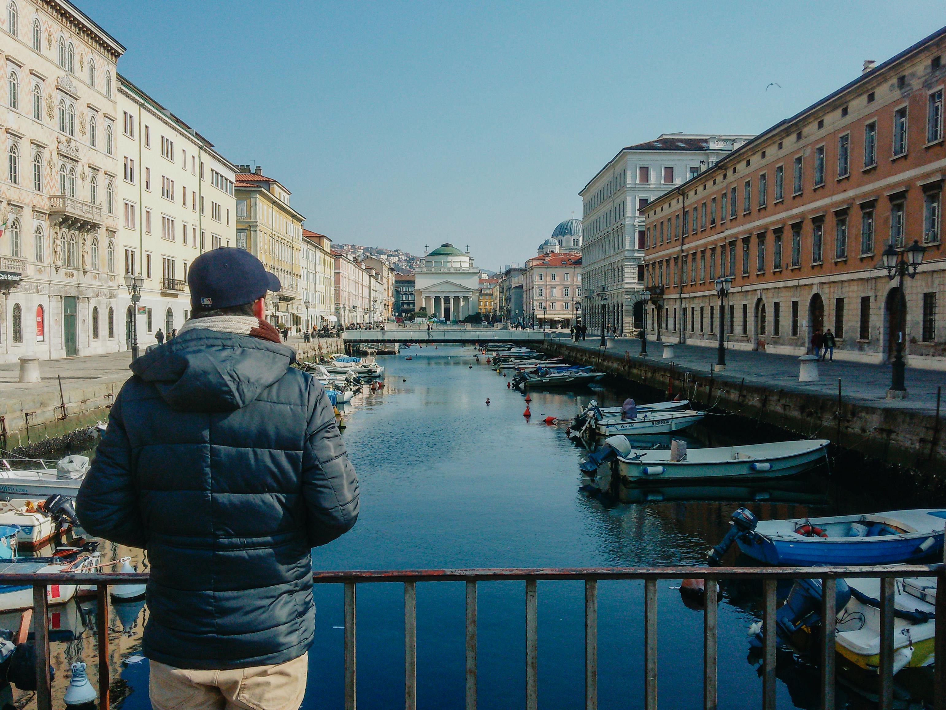 Zadarmo Osoba v bunde pozoruje malebný mestský kanál s farebnými budovami a kotviacimi loďami pod jasnou oblohou. Fotka z fotobanky