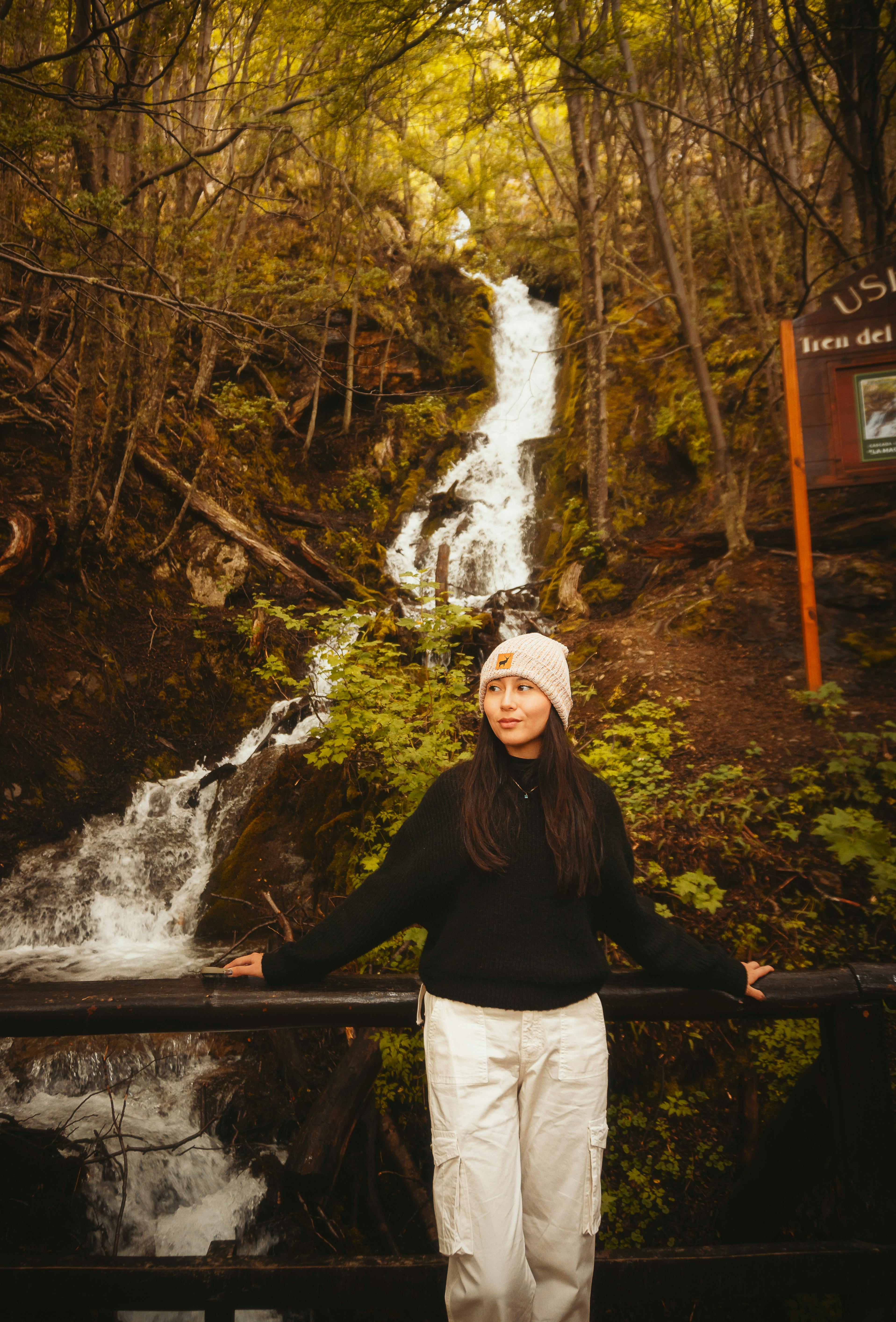 免费 一位年轻女子站在乌斯怀亚风景秀丽的瀑布旁，周围绿树环绕。 素材图片