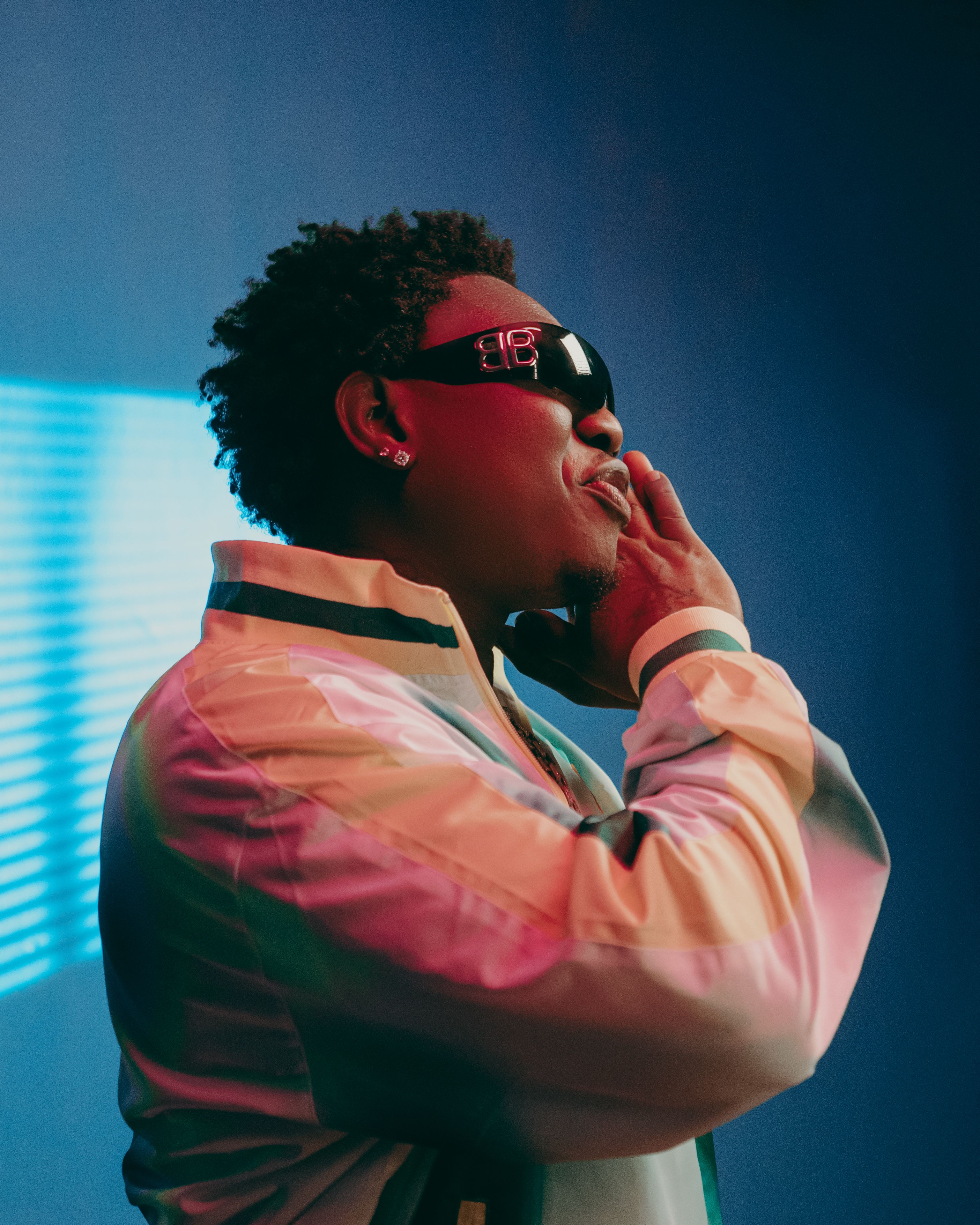 Fashionable adult male in sunglasses under neon lighting, side view.