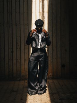 A fashionable individual wearing a stylish outfit stands in dramatic lighting, casting shadows.