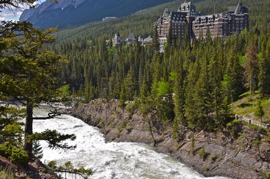 View of Banff Springs Hotel nestled in lush forest by river, Canadian Rockies.