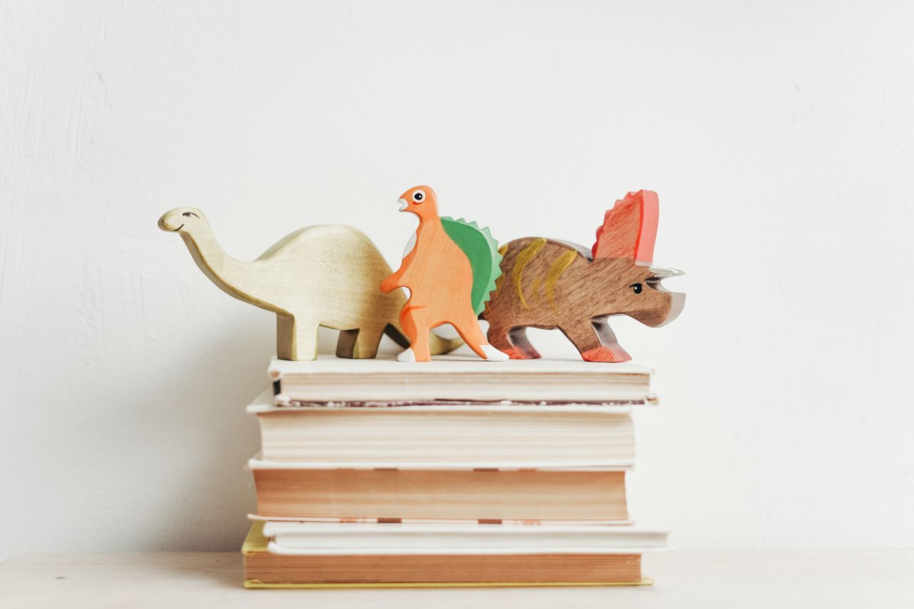 Dinosaurus kayu berwarna-warni di atas tumpukan buku