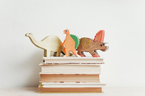 Free Colorful wooden dinosaurs on top of a stack of hardcover books on a light background. Stock Photo