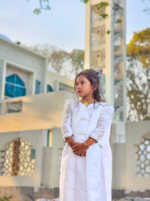 Free A girl in traditional attire stands near a mosque with intricate architecture, exuding cultural elegance. Stock Photo