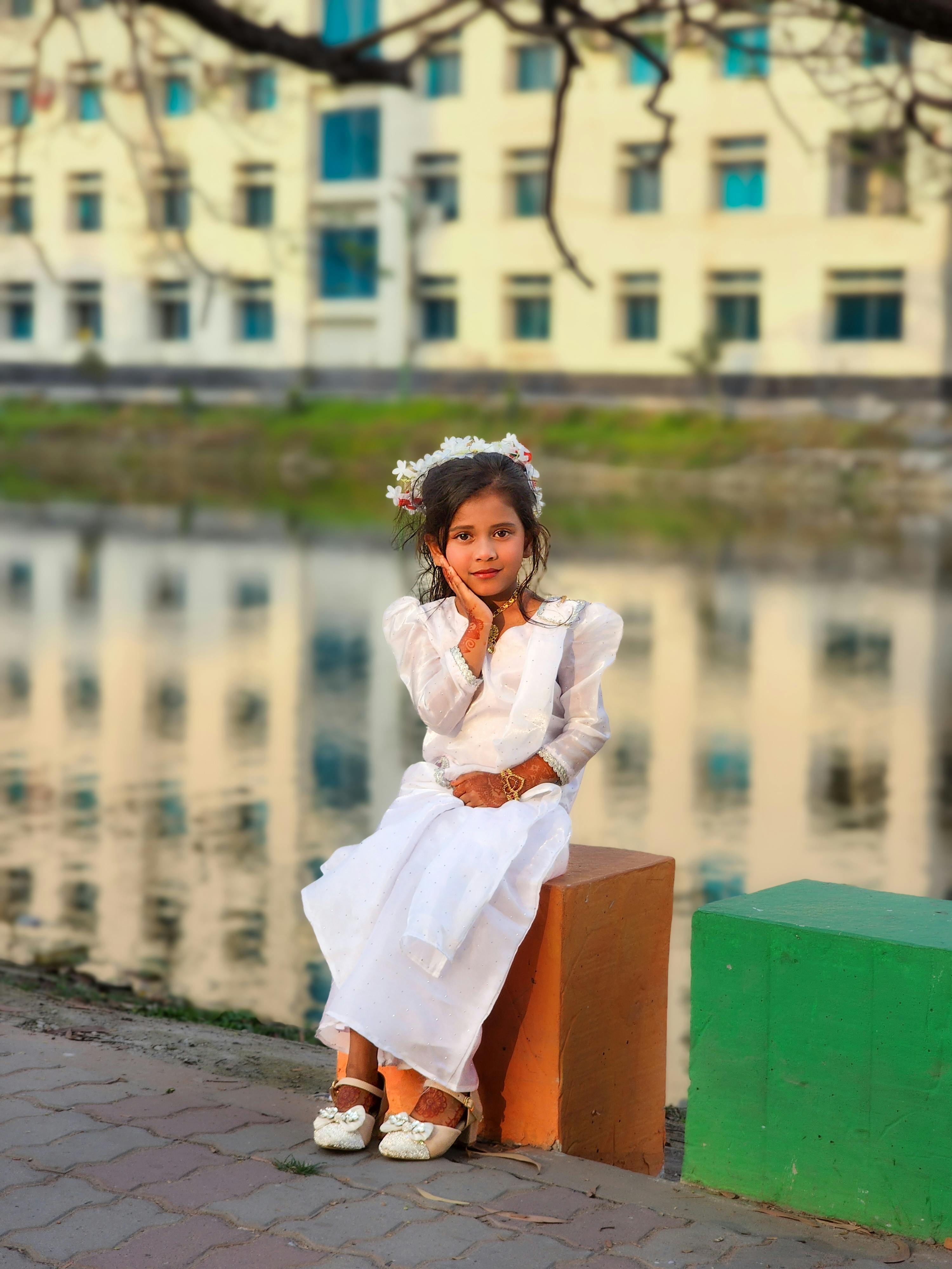Zadarmo Mladé dievča elegantne oblečené v bielom sedí pri rieke s odrazom budovy v pozadí. Fotka z fotobanky