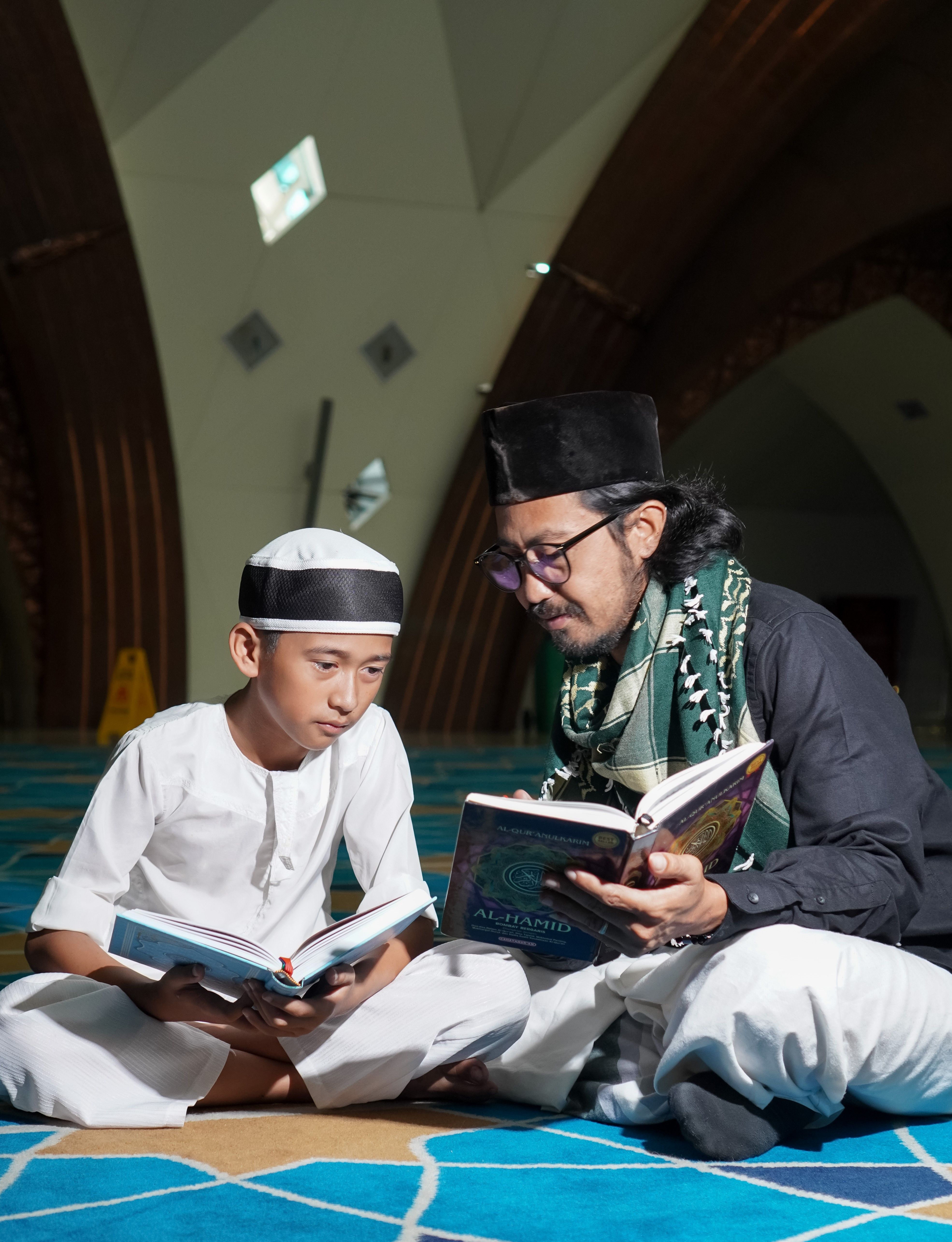 A father and son reading religious texts together in an Indonesian mosque.