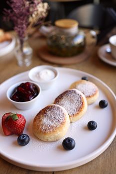 Appetizing pancakes with berries and cream, served with tea, evoke a cozy breakfast.