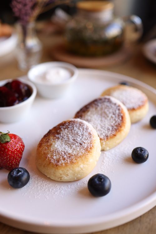 Free Tasty syrniki served with strawberries, blueberries, and cream, perfect for breakfast. Stock Photo