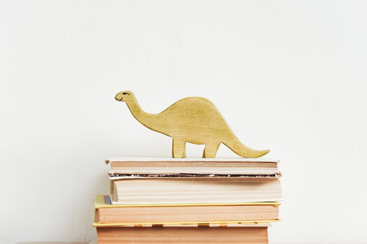 Brown Wooden Dinosaur Figurine On White Book