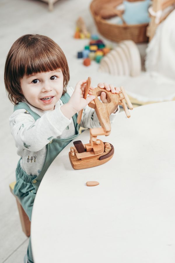 Little girl in a yellow dress playing with a wooden train on green carpet