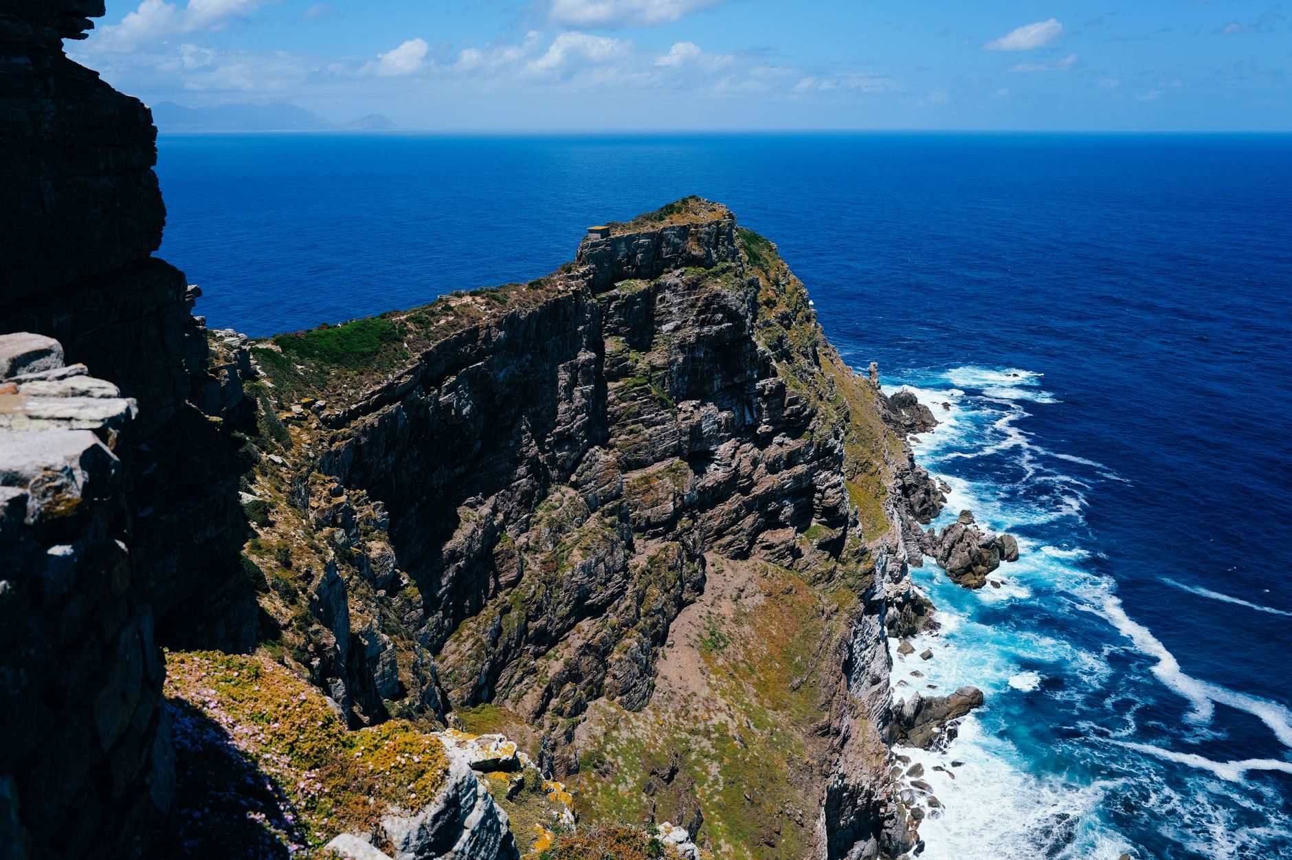 Impresionante vista de los escarpados acantilados de Cape Point encontrándose con las azules olas del océano bajo un cielo despejado.