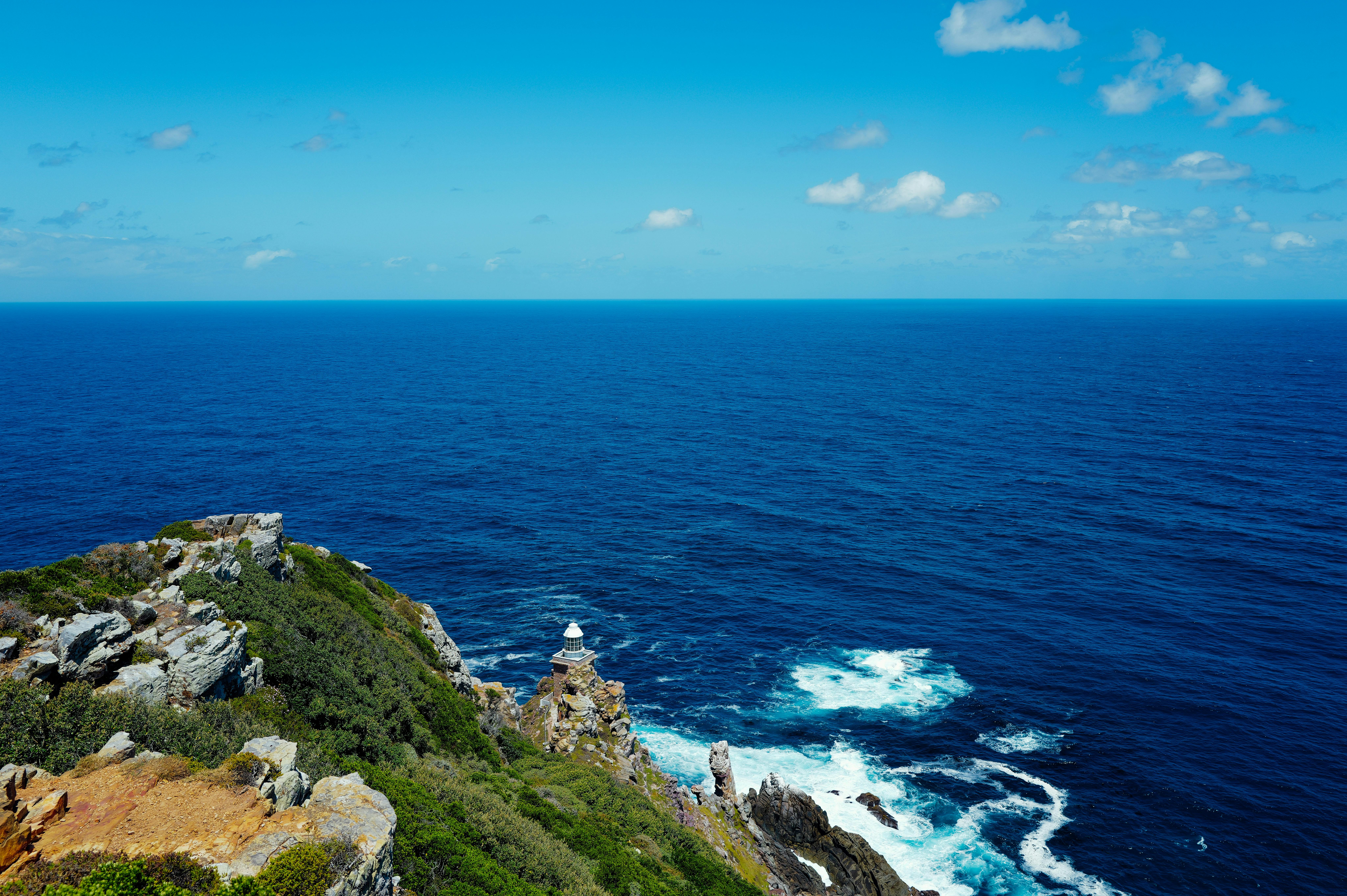 免费 一座灯塔矗立在岩石峭壁上，俯瞰着蔚蓝天空下浩瀚宁静的大海。 素材图片