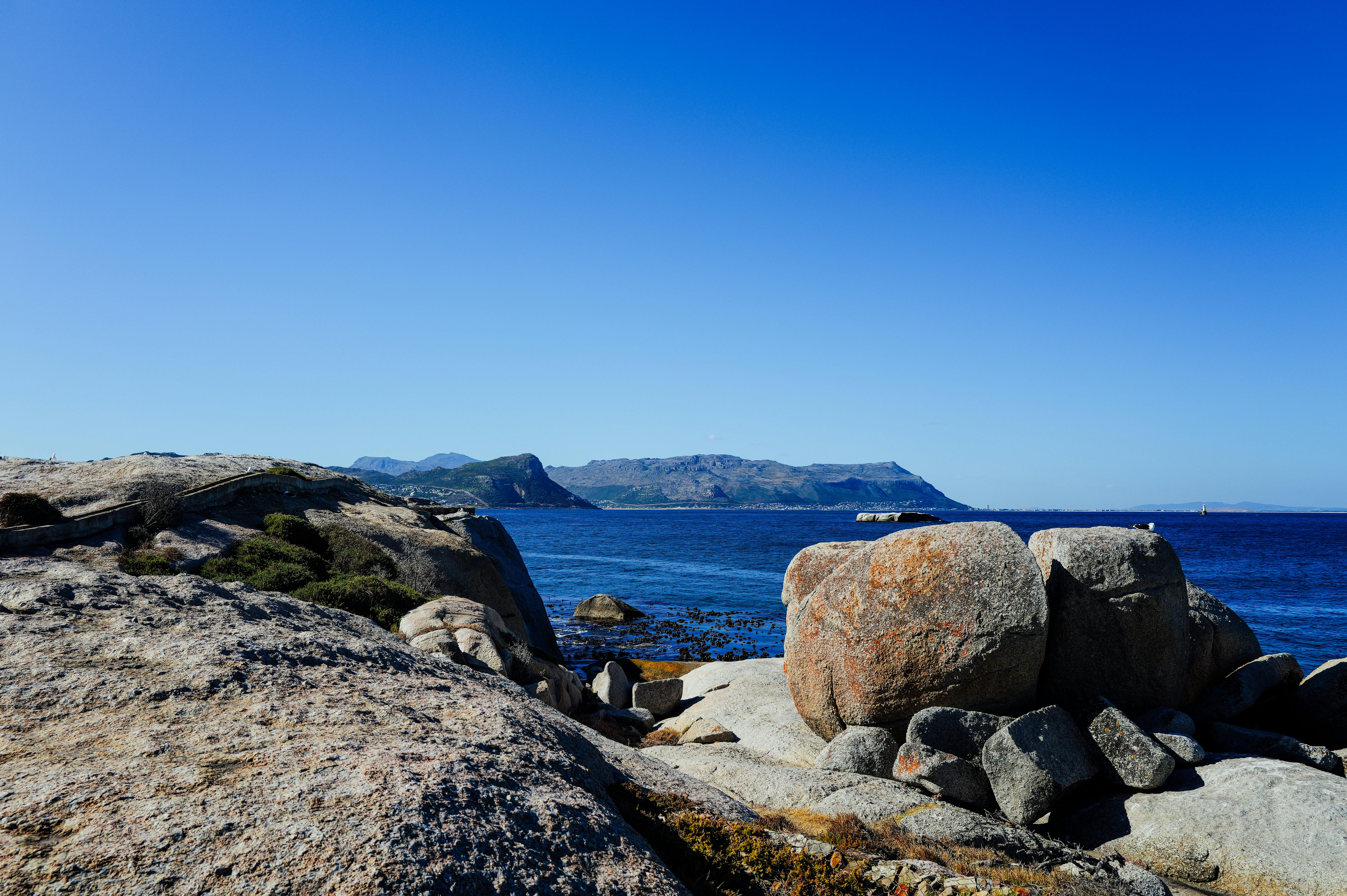 Zadarmo Krásne skalnaté pobrežie s jasnou modrou oblohou a vzdialenými horami pod jasným slnečným svetlom. Fotka z fotobanky