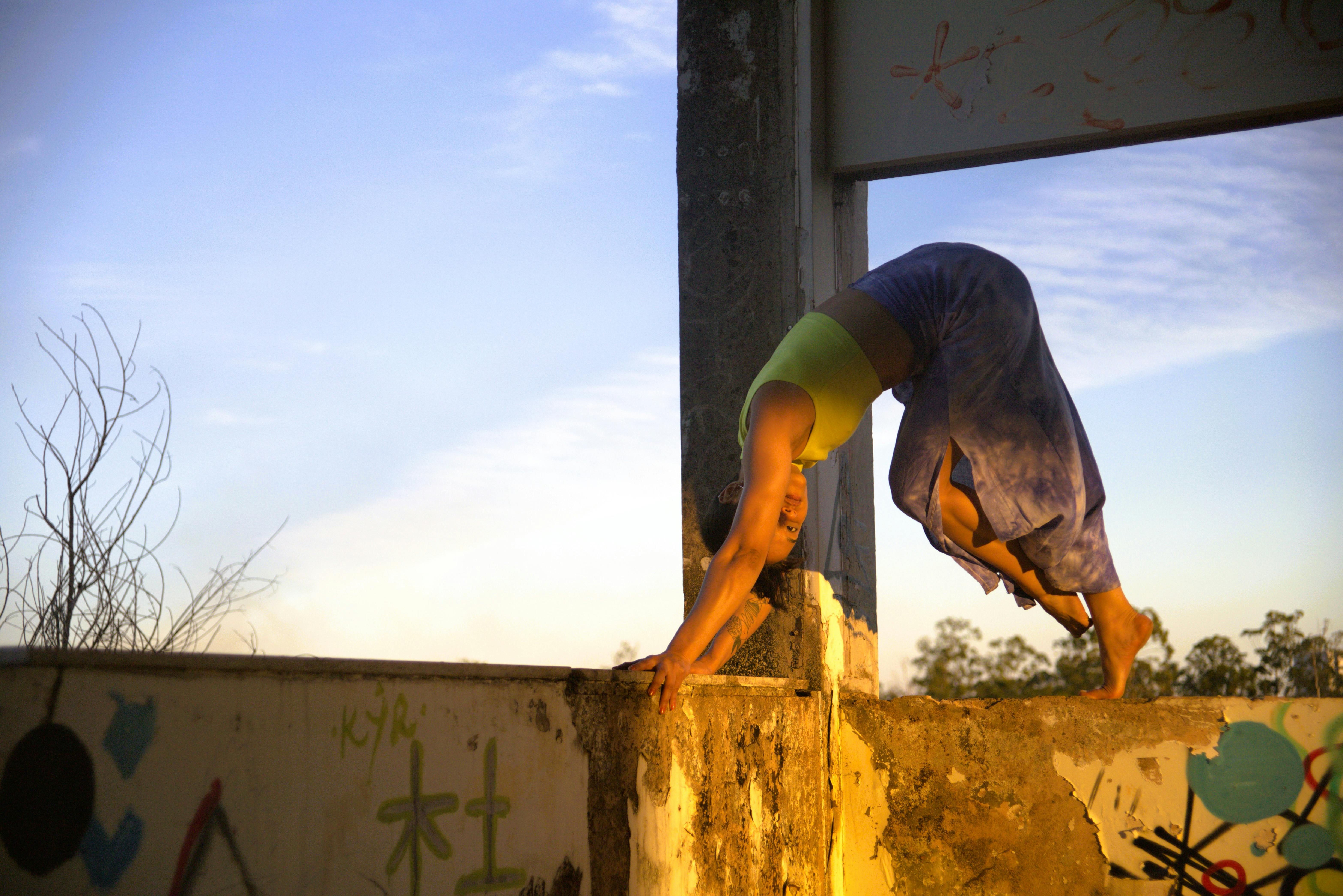 Безкоштовне Жінка граціозно виконує стійку на руках на стіні на тлі заходу сонця. стокове фото