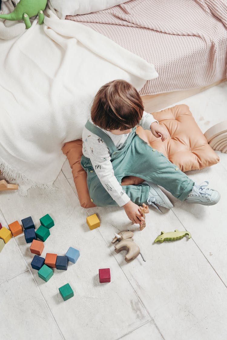  Child In White Long-sleeve Top And Dungaree Trousers Playing With Toys