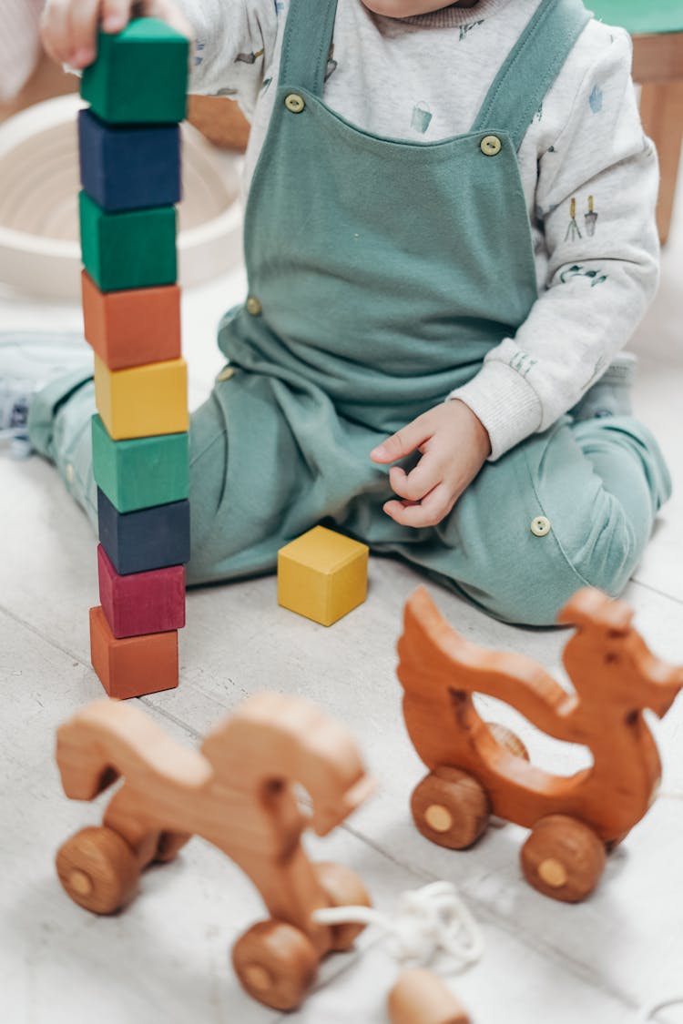 Child In White Long-sleeve Top And Dungaree Trousers  Playing With Lego Blocks