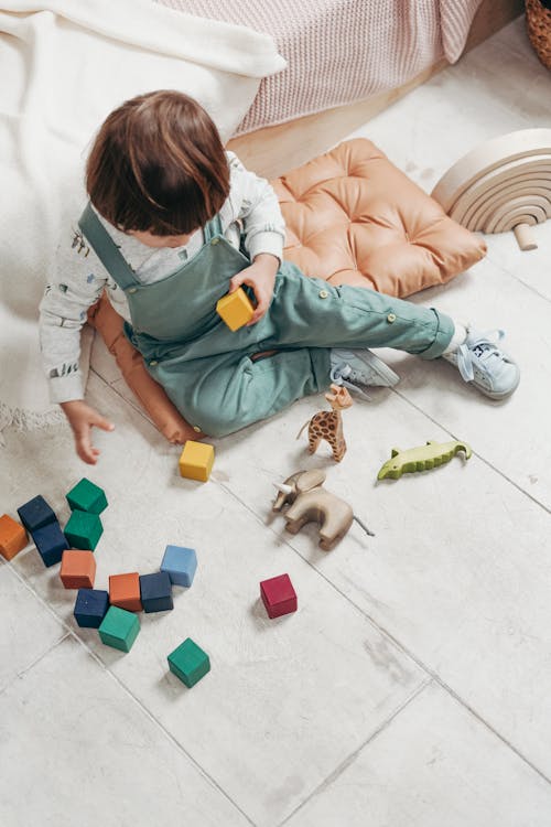 白い長袖のトップとレゴブロックで遊ぶダンガリーのズボンの子供