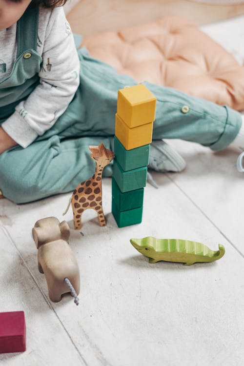 ребенок в белом топе с длинными рукавами и комбинезонах играет с кубиками Lego