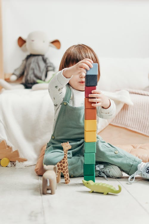 ребенок в белом топе с длинными рукавами и комбинезонах играет с кубиками Lego