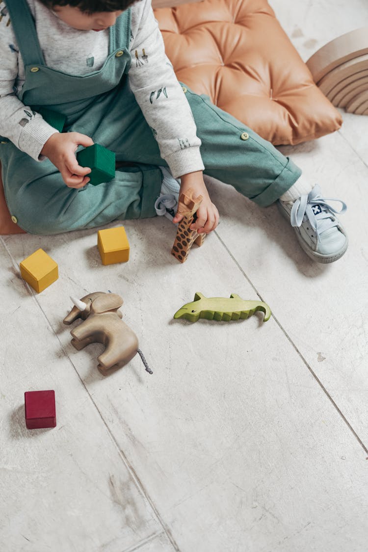 Child In White Long-sleeve Top And Dungaree Trousers Playing With Lego Blocks