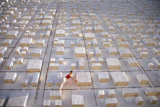A woman artistically poses on a concrete block grid outdoors, showcasing balance and creativity.