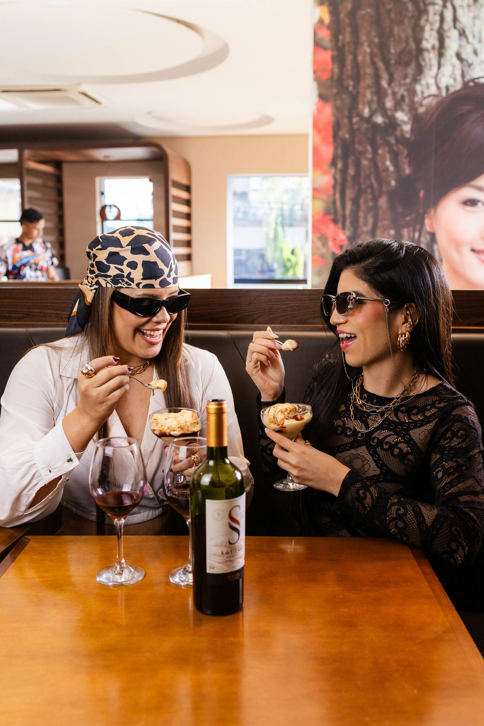 Two stylish women enjoy dessert and wine in a modern restaurant setting, exuding elegance and friendship.