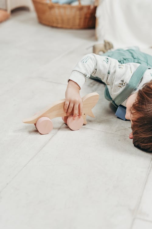 白い長袖トップの子供と木のおもちゃで遊んで横たわっているダンガリーのズボン