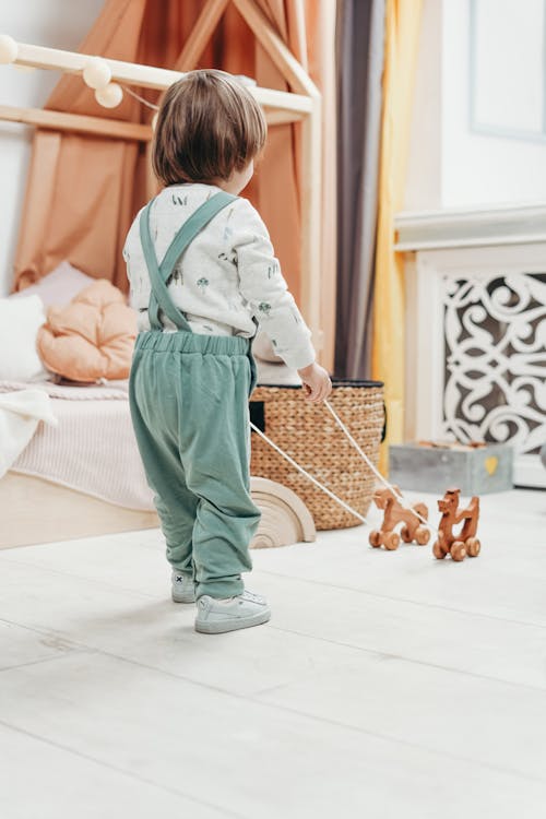ребенок в белом топе с длинными рукавами и брюках комбинезоне играет с деревянными игрушками