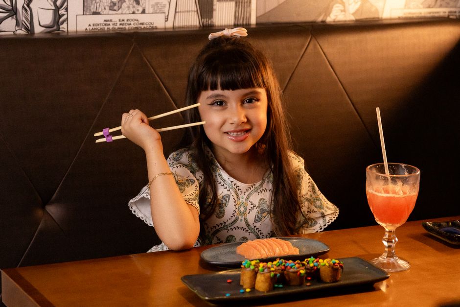 Como a Criatividade Pode Enriquecer sua Alimentação Saudável 2 Charming young girl in a restaurant using chopsticks, enjoying sushi and a colorful dessert.
