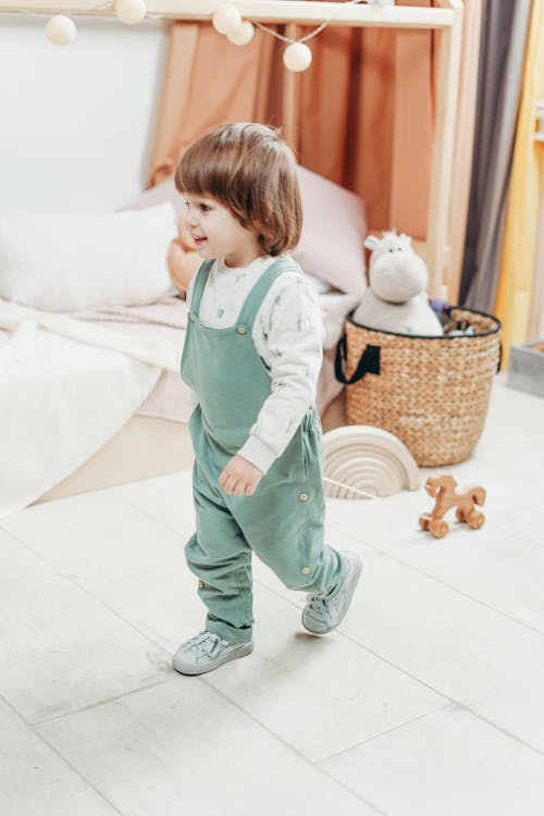 木のおもちゃで遊ぶ白い長袖のトップと緑のダンガリーのズボンの子供