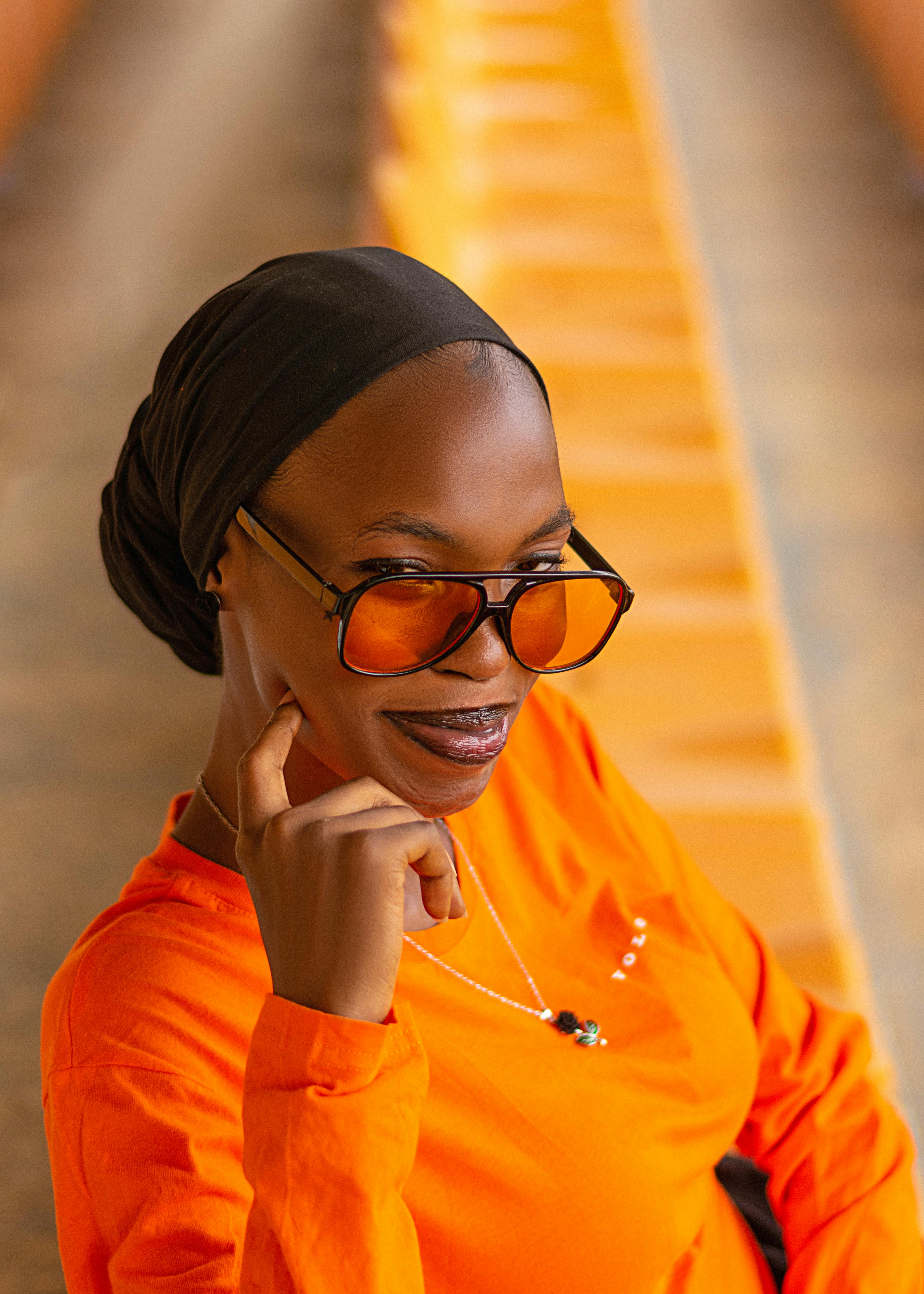 Безкоштовне Портрет стильної жінки в помаранчевому вбранні та сонцезахисних окулярах, що випромінює впевненість. стокове фото