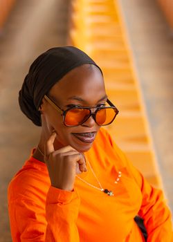 Portrait of a stylish woman in an orange outfit and sunglasses, exuding confidence.