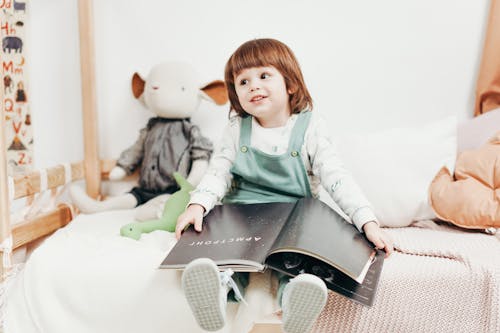 Bambino In Cima A Manica Lunga Bianca Che Si Siede Sul Letto Che Tiene Il Libro