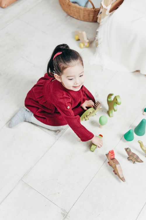 Free A joyful child in a red dress plays with wooden toys on a light floor. Perfect for childhood themes. Stock Photo