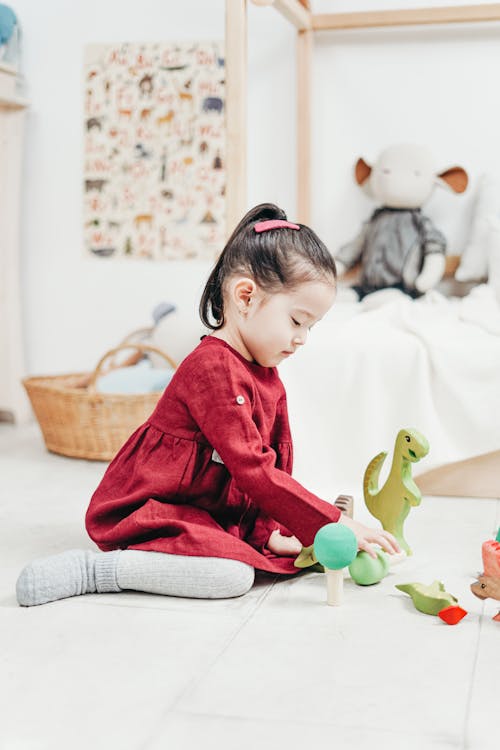 おもちゃで遊ぶ白い床タイルに座っている赤い長袖のドレスの女の子