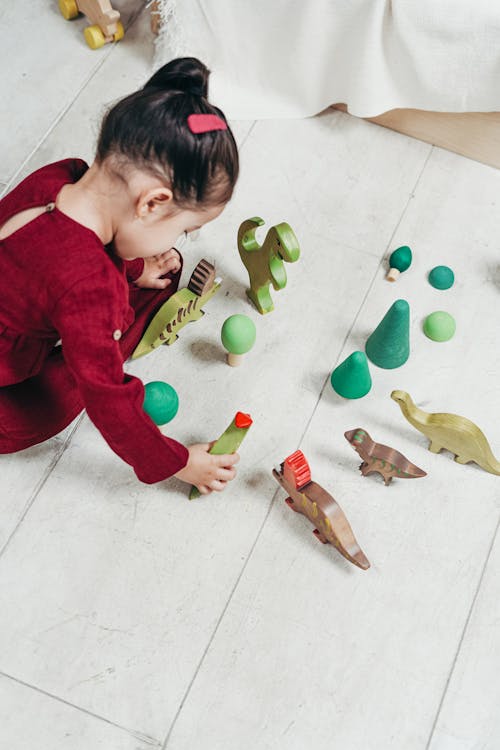 Fille En Robe à Manches Longues Rouge Assis Sur Des Carreaux De Sol Blanc Jouant Avec Des Jouets