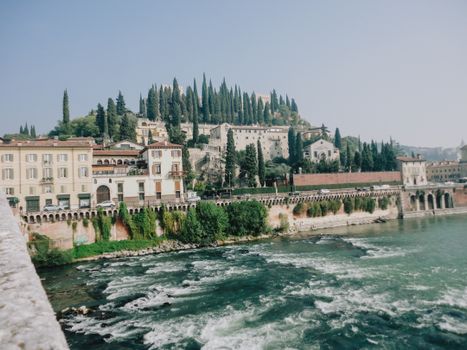 Beautiful photograph capturing Castel San Pietro in Verona, Italy with lush greenery and flowing river.