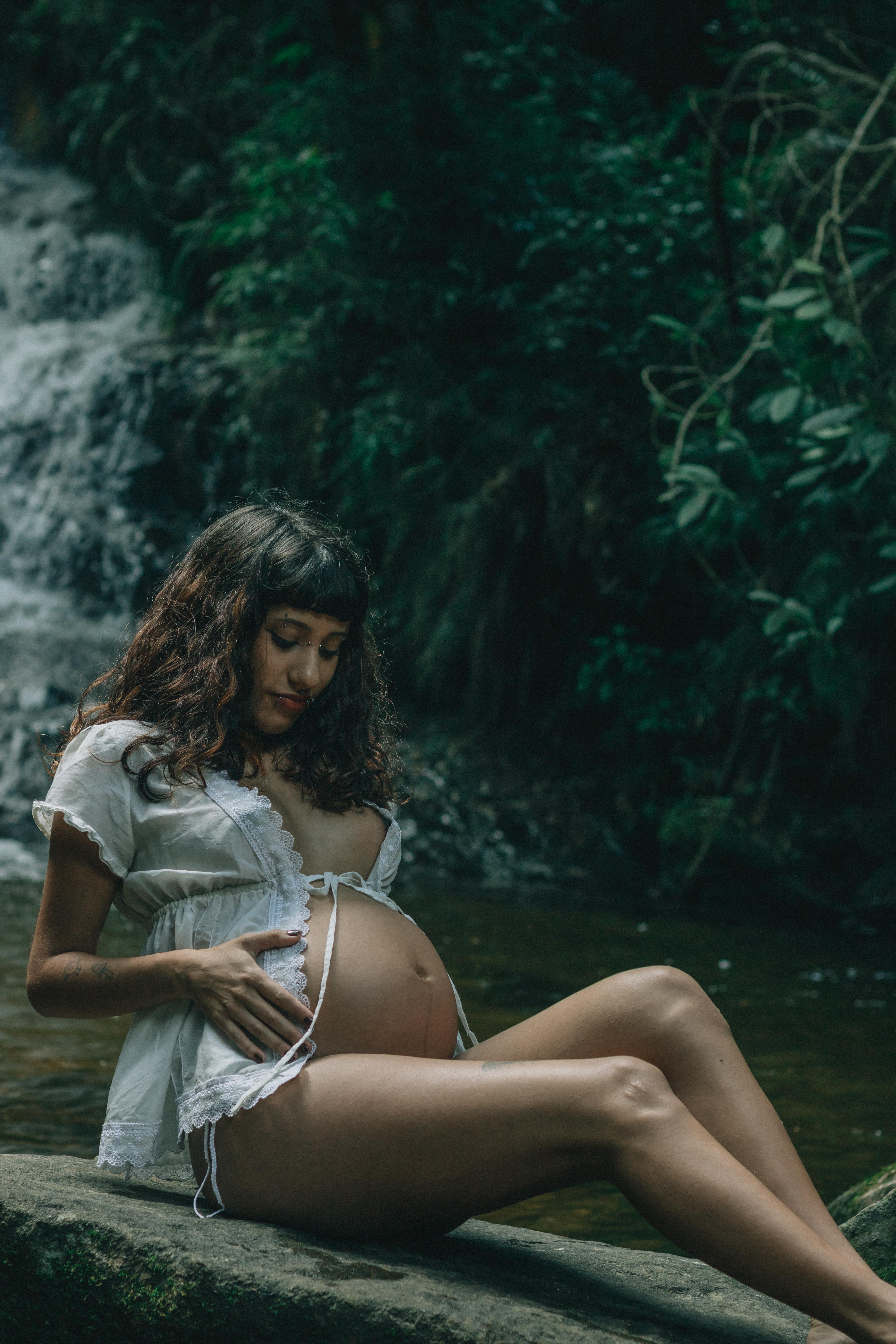 免費 一位身穿白衣的孕婦靜靜地坐在瀑布旁。 圖庫相片