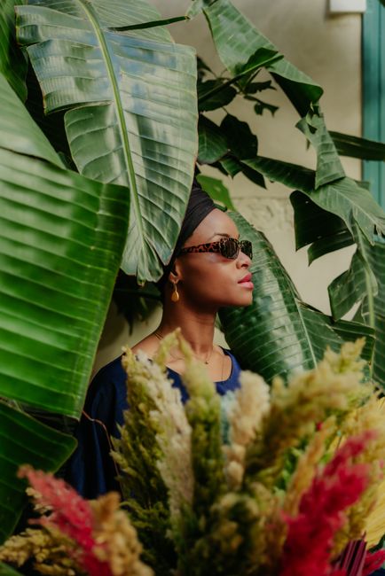 A stylish woman in sunglasses amidst lush tropical leaves and vibrant florals in Morocco.