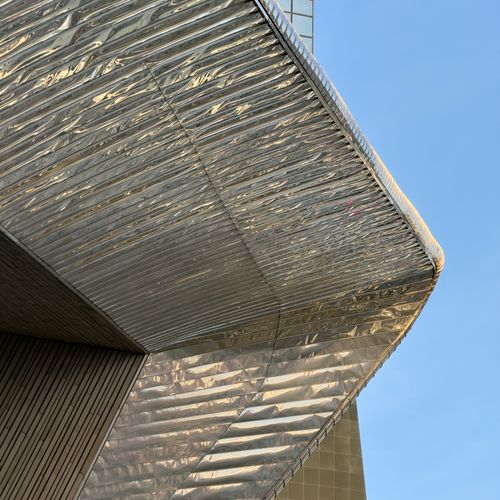 Free Close-up of modern architecture featuring a shiny, metallic facade against a clear blue sky. Stock Photo
